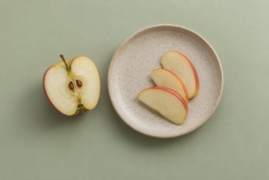 An apple core with visible seeds sits apart from thin apple slices on a stoneware plate.