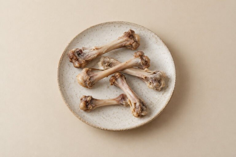 Cooked chicken bones rest on a plain stoneware plate against a warm neutral backdrop.